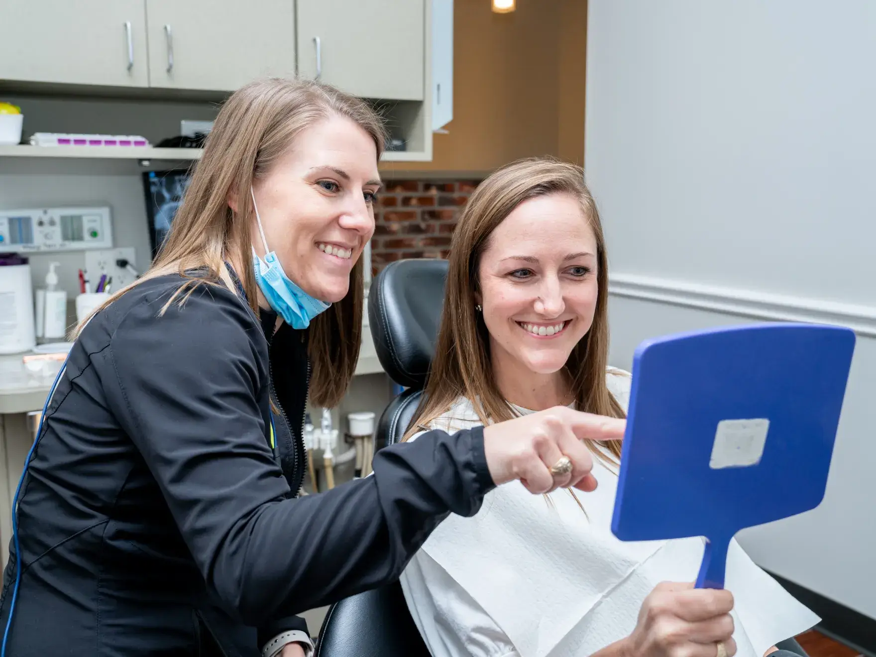 two women sitting in a dentist chair holding a mirror